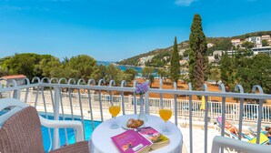 A poolside table with books, croissants, and orange juice glasses, overlooking a pool and a coastal town. - Hotel Komodor (Dubrovnik)