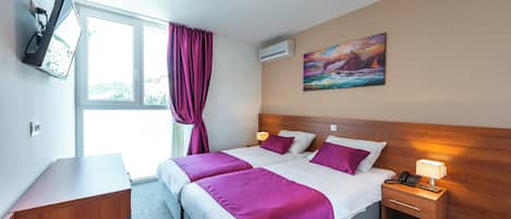 Quarto de hotel com cama, mesa de cabeceira com abajur, televisão na parede e um quadro na parede.