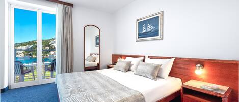 Une chambre d’hôtel avec un grand lit, une table de chevet, un miroir et une vue sur la mer, accessible par une porte coulissante.