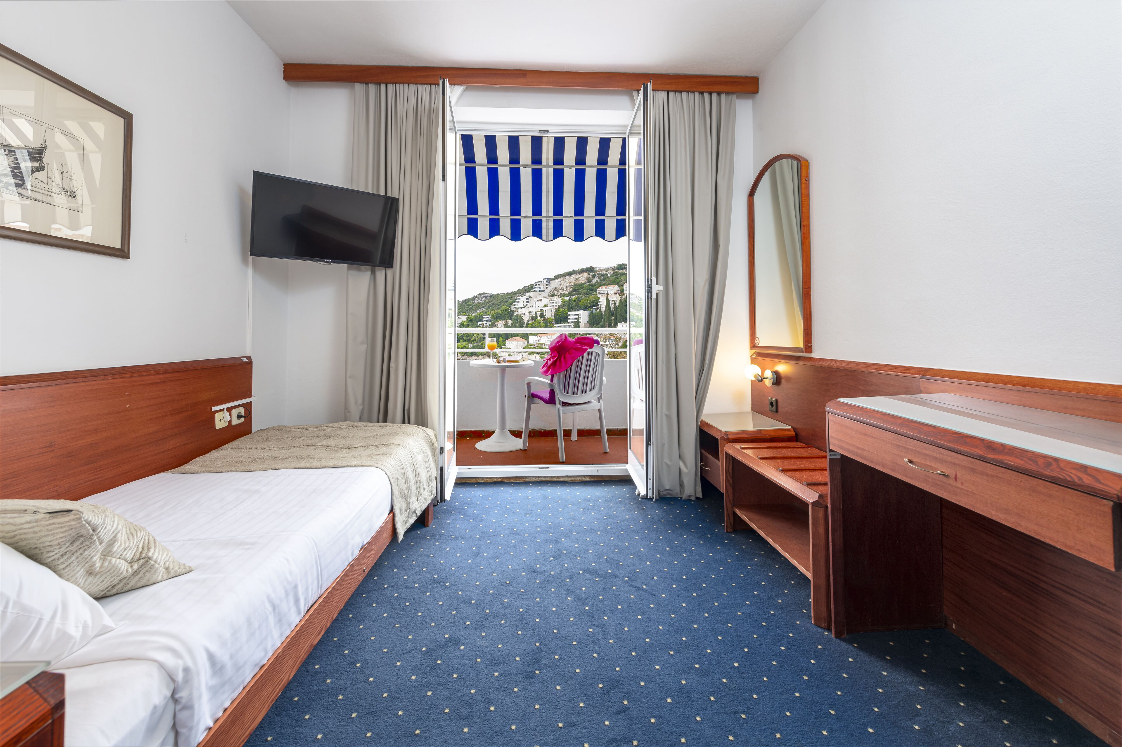 A hotel room with a bed, a desk, a TV, a balcony with a view of the city, and a window with curtains.