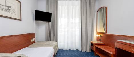 Una habitación de hotel con una cama, televisión, escritorio, espejo y ventana con cortinas.