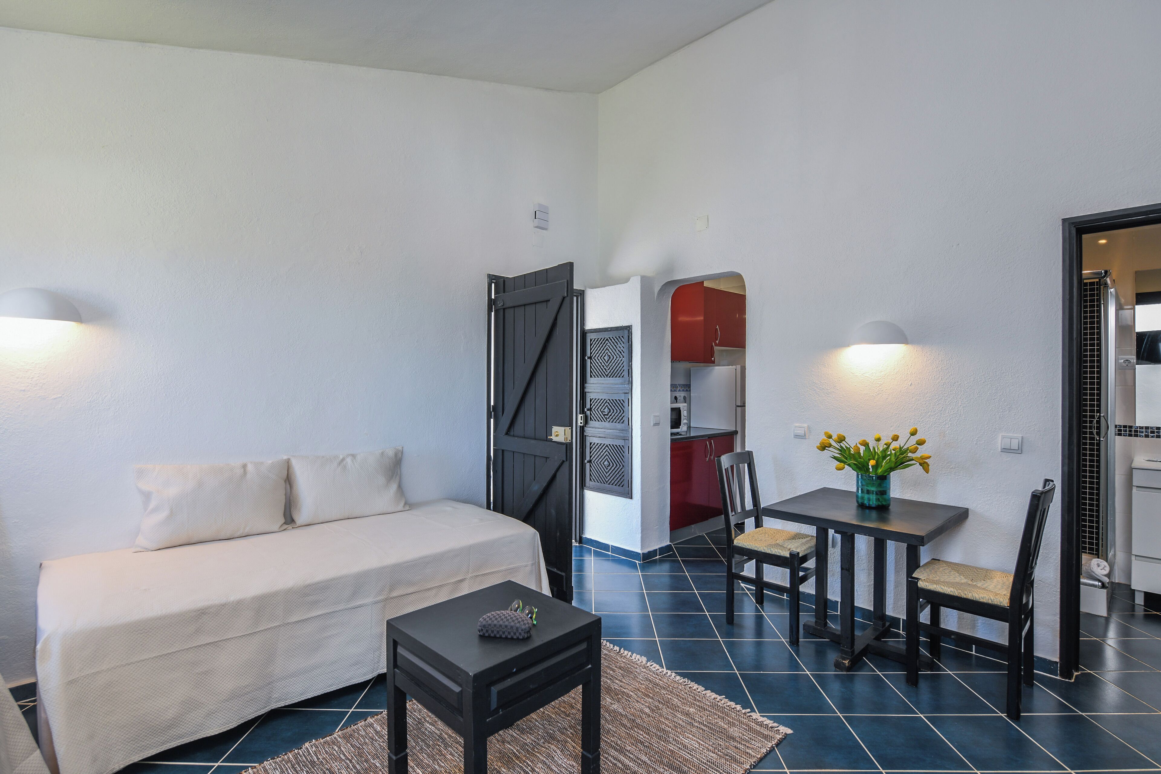Un espacio habitable compacto con un sofá, una mesita, una silla y una kitchenette al fondo.