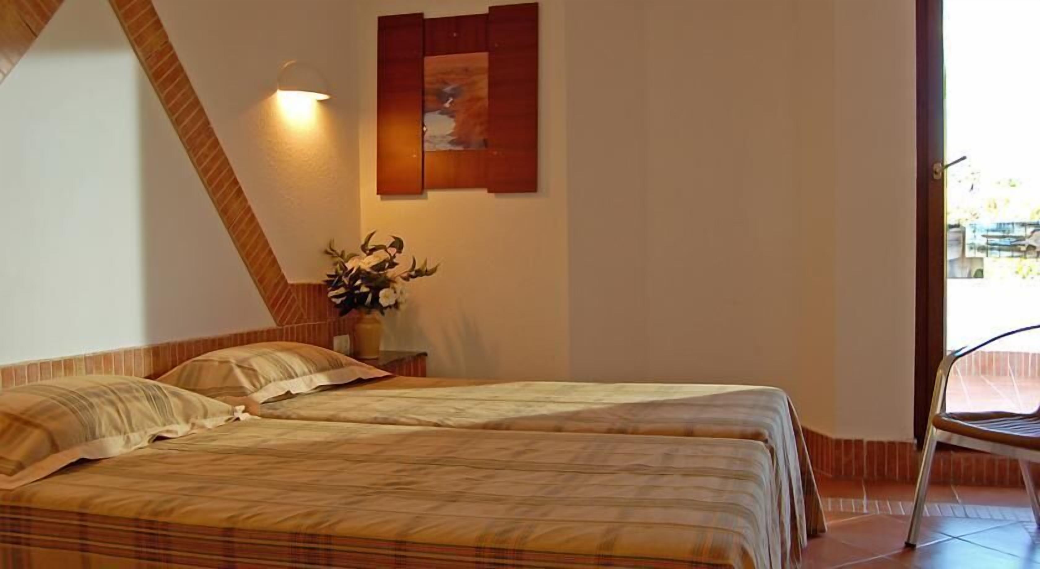 Une chambre avec deux lits, une lampe fixée au mur, un tableau et une plante en pot.