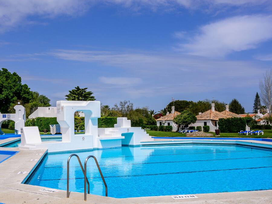 A clear blue swimming pool with steps leading into it, surrounded by white structures and greenery.