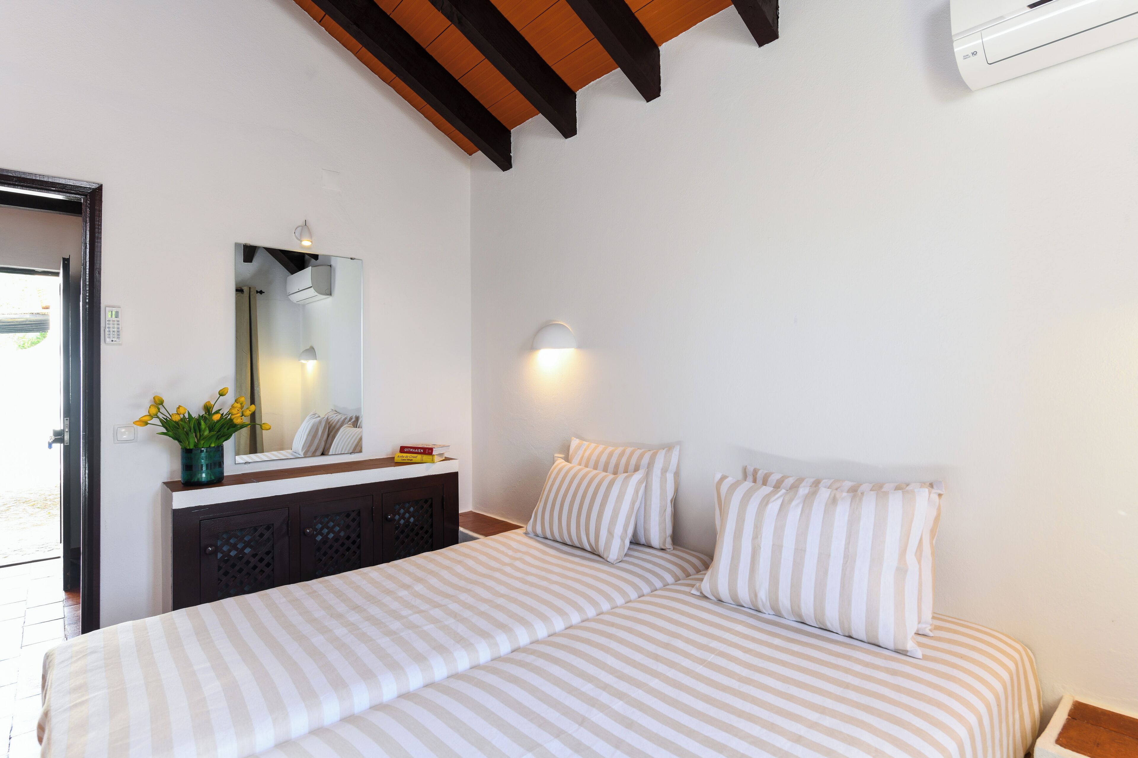 Un dormitorio con cama, mesita de noche, espejo y lámpara de pared.