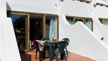 Une terrasse extérieure avec une table et des chaises, une porte-fenêtre coulissante et un petit jardin.