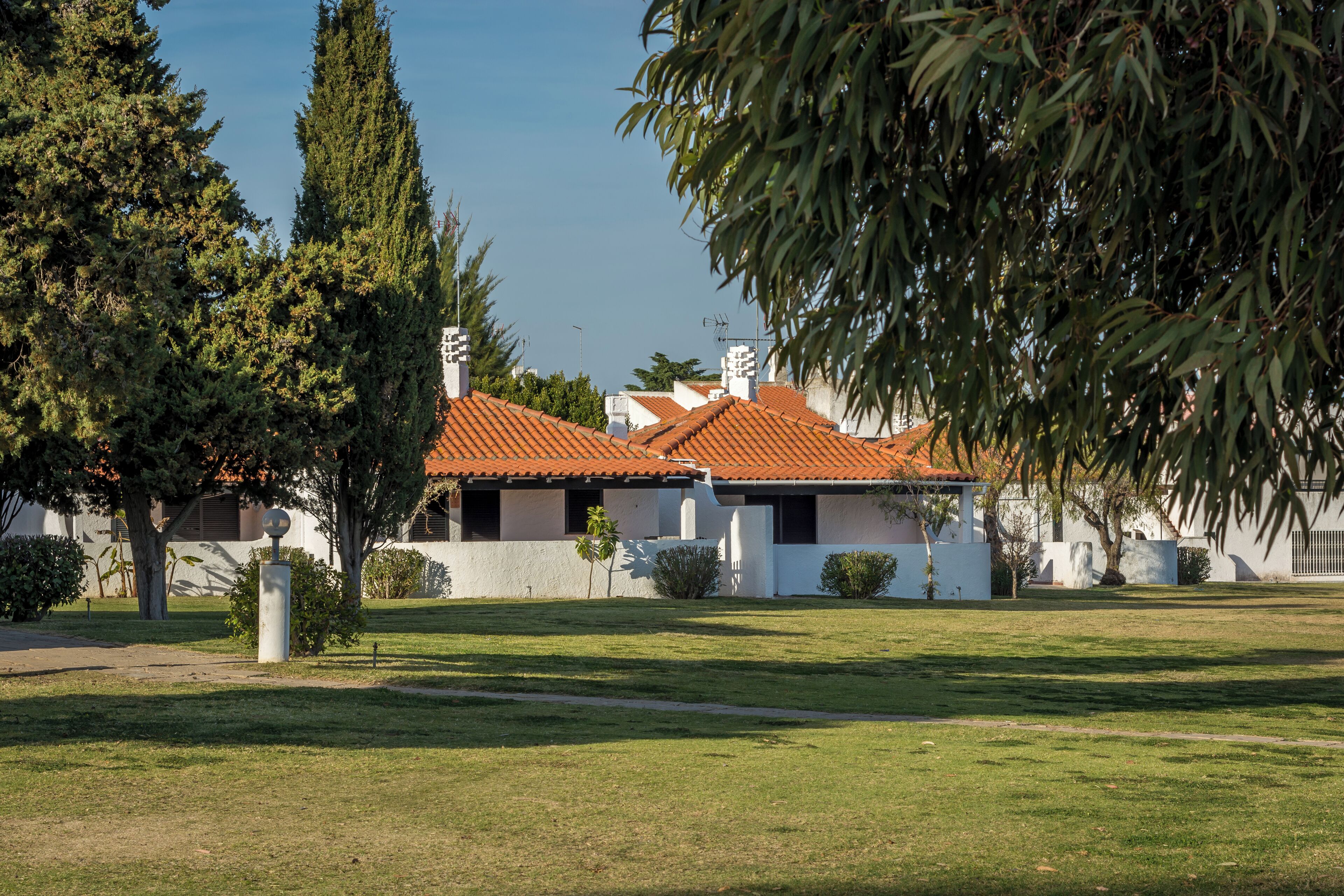 A building with a red-tiled roof, surrounded by a grassy area and trees.