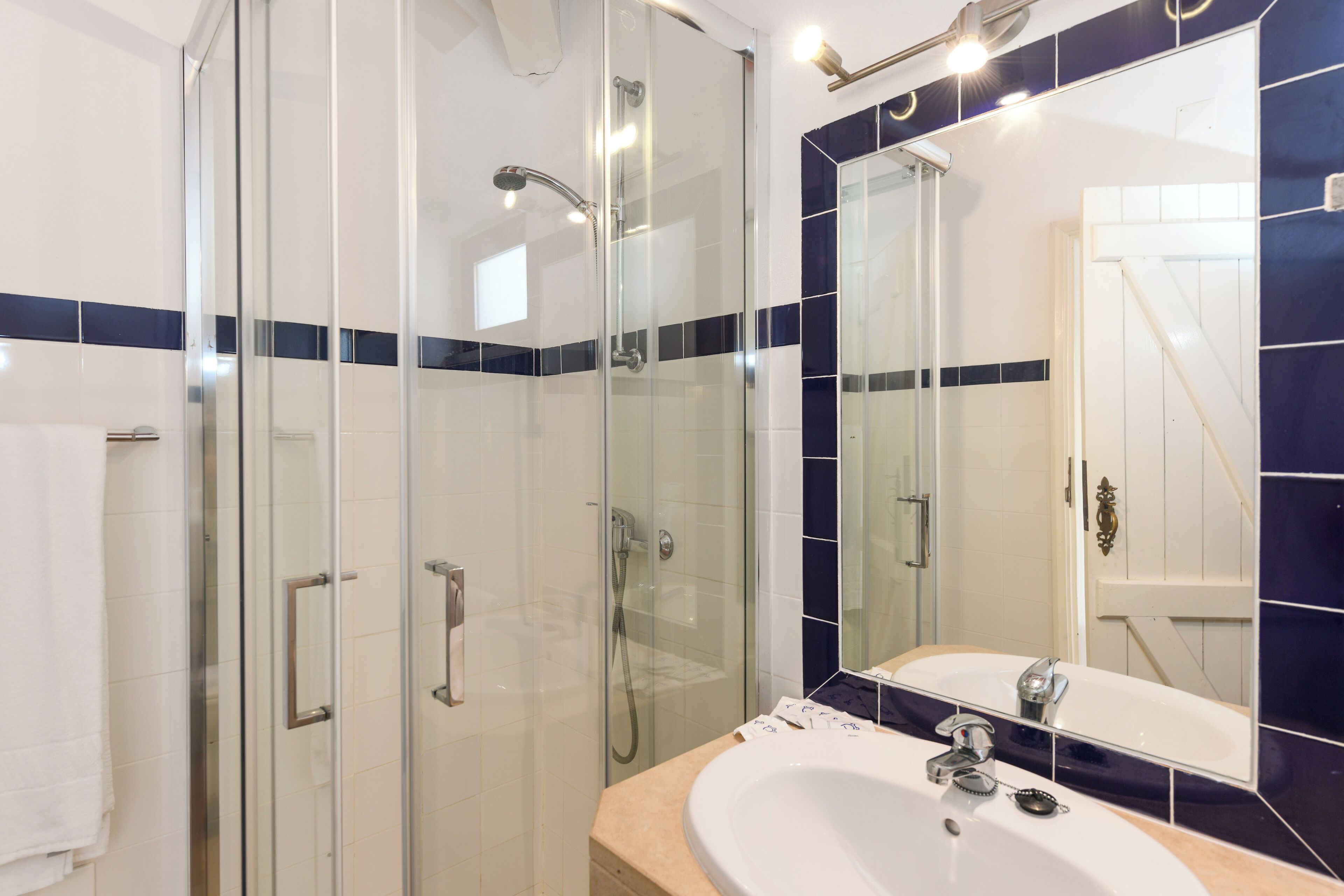 A modern bathroom with a glass-enclosed shower, a large mirror, and a beige countertop.