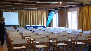 A conference room with rows of wooden chairs, a projector screen, and a blue banner with text.