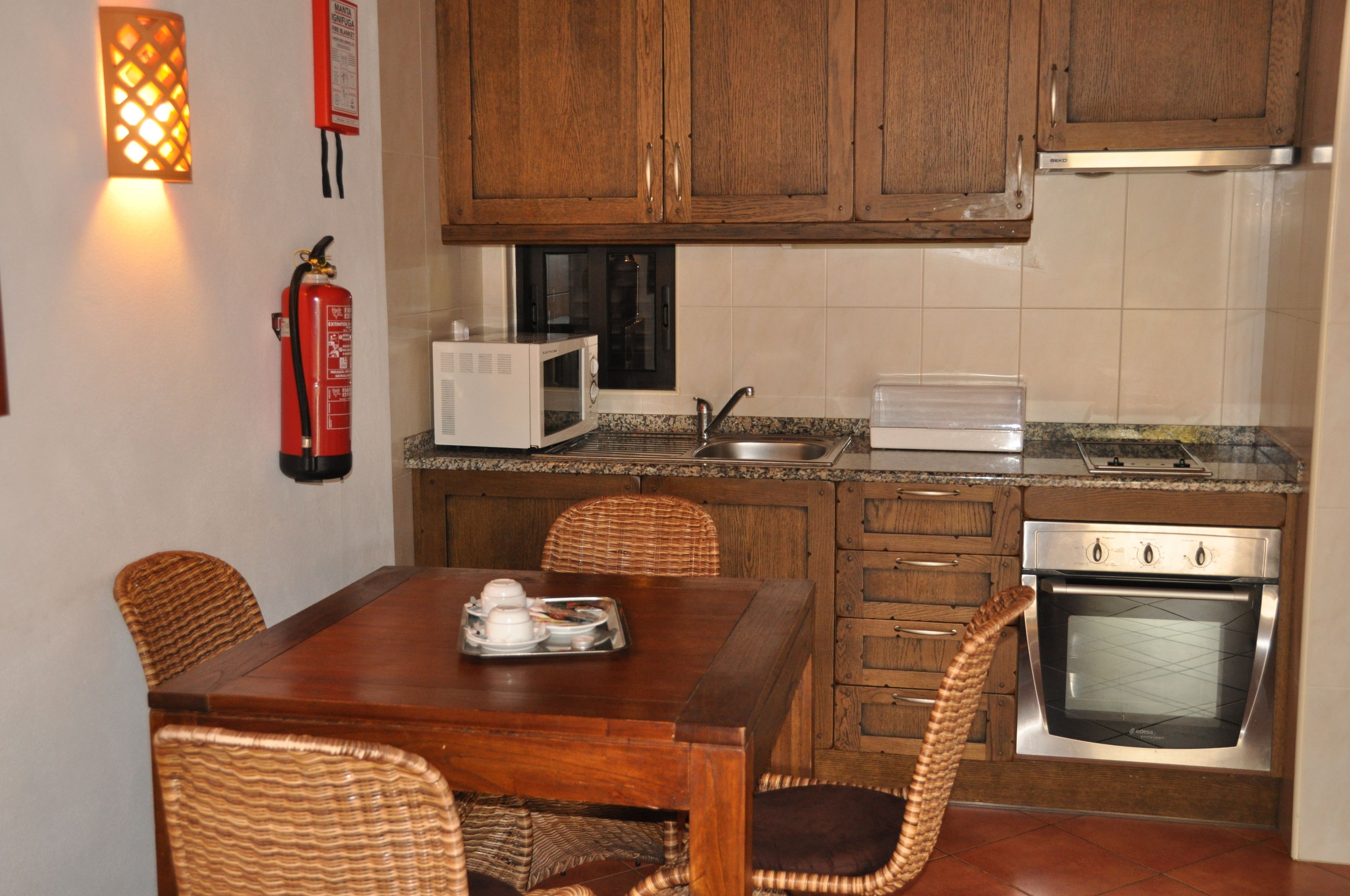 A compact kitchen with wooden cabinets, a microwave, a stove, and a dining area with wicker chairs.