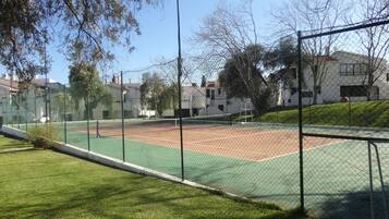 Een tennisbaan omringd door een hek van gaas, met gebouwen en bomen op de achtergrond.