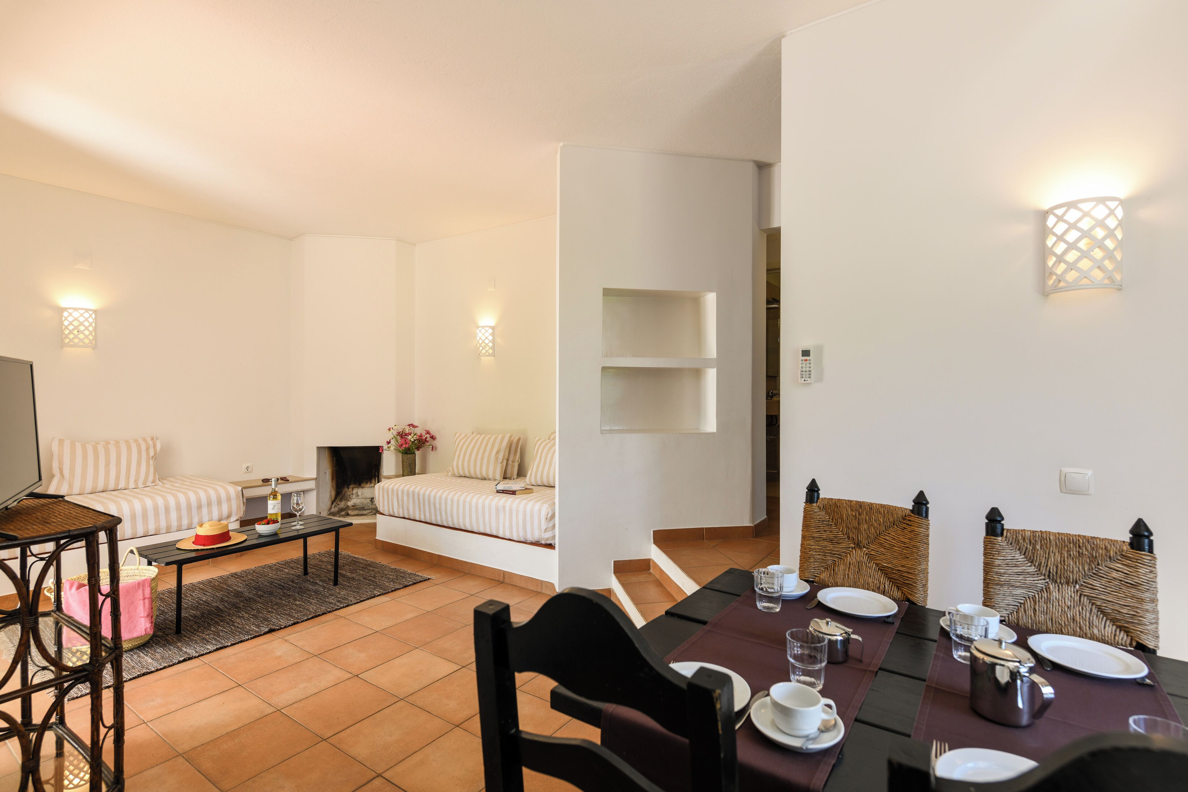 Ein modernes Wohnzimmer mit einer Couch, einem Couchtisch und einem Fernseher. Es gibt einen Essbereich mit einem Tisch für zwei Personen, Stühlen und einem Kamin.