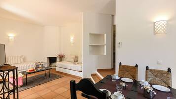 Ein modernes Wohnzimmer mit einer Couch, einem Couchtisch und einem Fernseher. Es gibt einen Essbereich mit einem Tisch für zwei Personen, Stühlen und einem Kamin.