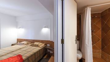 A bedroom with a bed, a nightstand, a bedside table, and a bathroom with a shower and toilet.