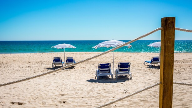 A beach with rows of blue and white striped beach umbrellas and lounge chairs. - Pedras d'el Rei (Tavira)