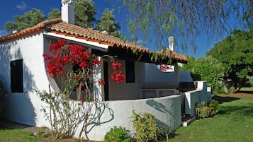 Un bâtiment blanc avec un toit recouvert de tuiles, un petit porche et des fleurs rouges devant.