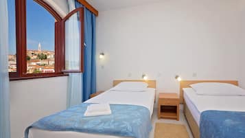 Habitación de hotel con dos camas, una ventana con cortinas y vistas a un paisaje urbano.