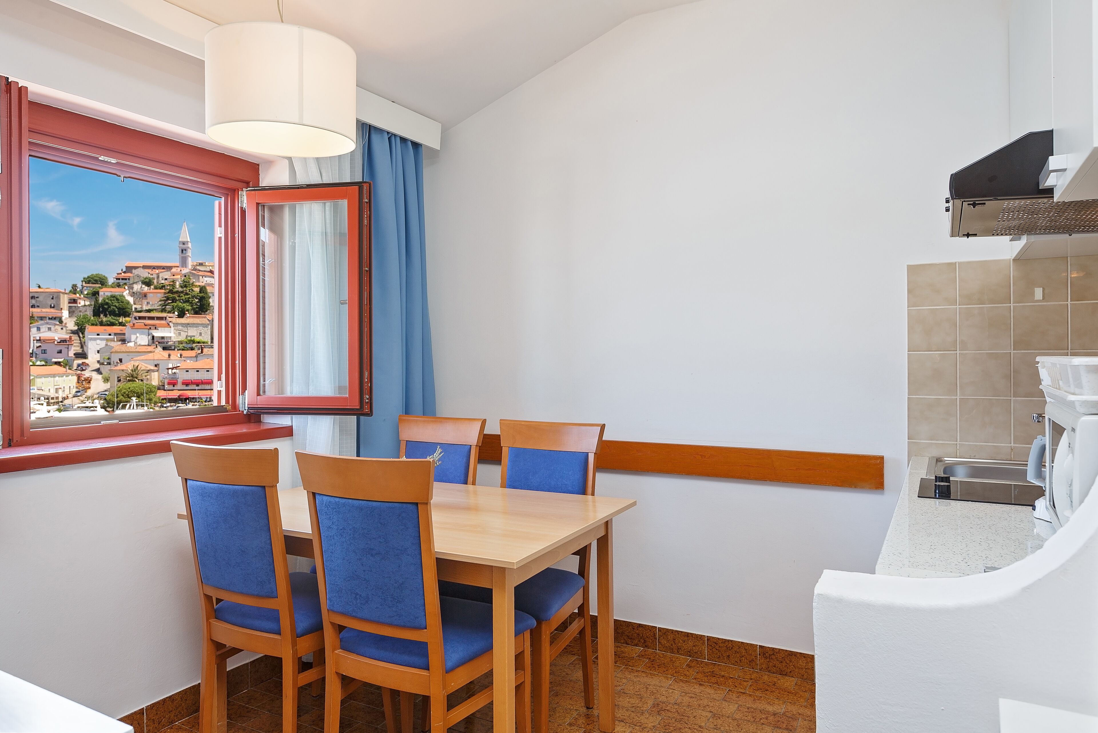 A compact kitchen with a dining area, a window with a view of a town, and a white sink.