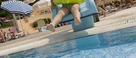A pool area with a water slide, lounge chairs, and umbrellas.