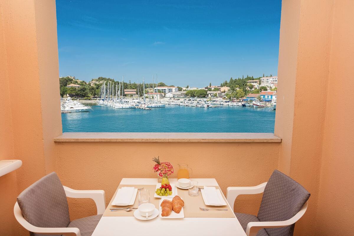 A balcony with a table set for breakfast, overlooking a marina with boats and buildings.