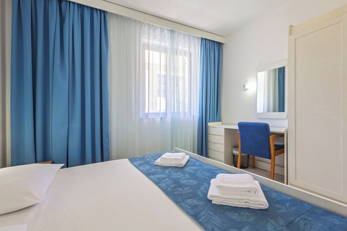 Hotellihuone, jossa on sänky, työpöytä ja tuoli.