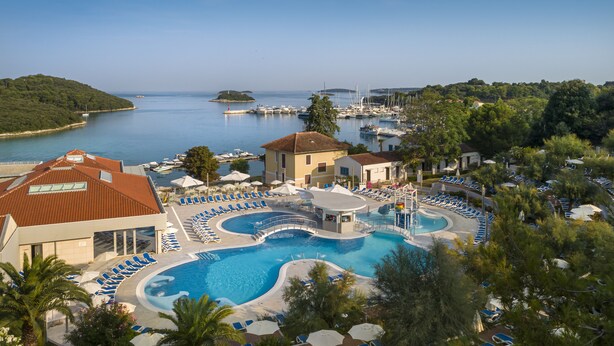 Un resort con una gran piscina, sillas de descanso y vista al mar.