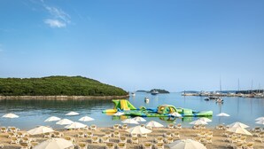 Una playa con sillas y sombrillas, un bote y una isla boscosa al fondo.