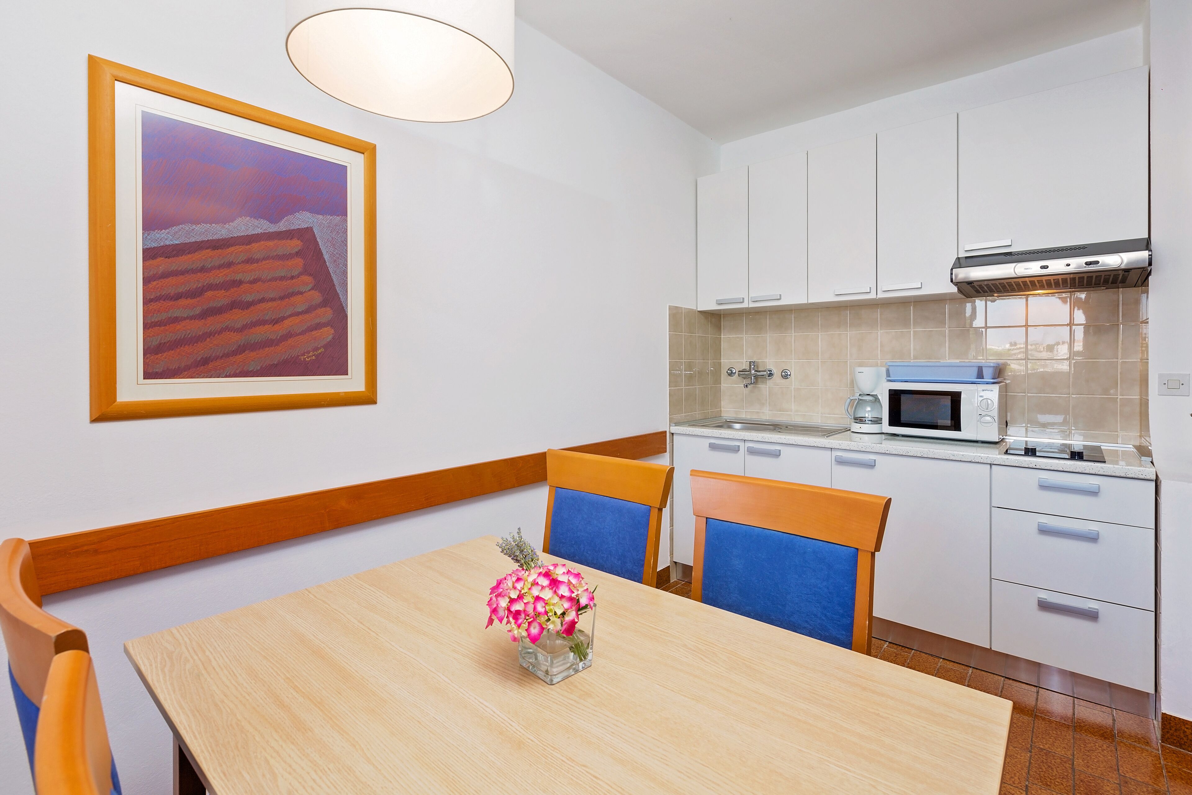 A modern kitchen with white cabinets, a microwave, and a stove. There is a dining table with chairs and a vase of flowers.