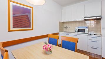A modern kitchen with white cabinets, a microwave, and a stove. There is a dining table with chairs and a vase of flowers.