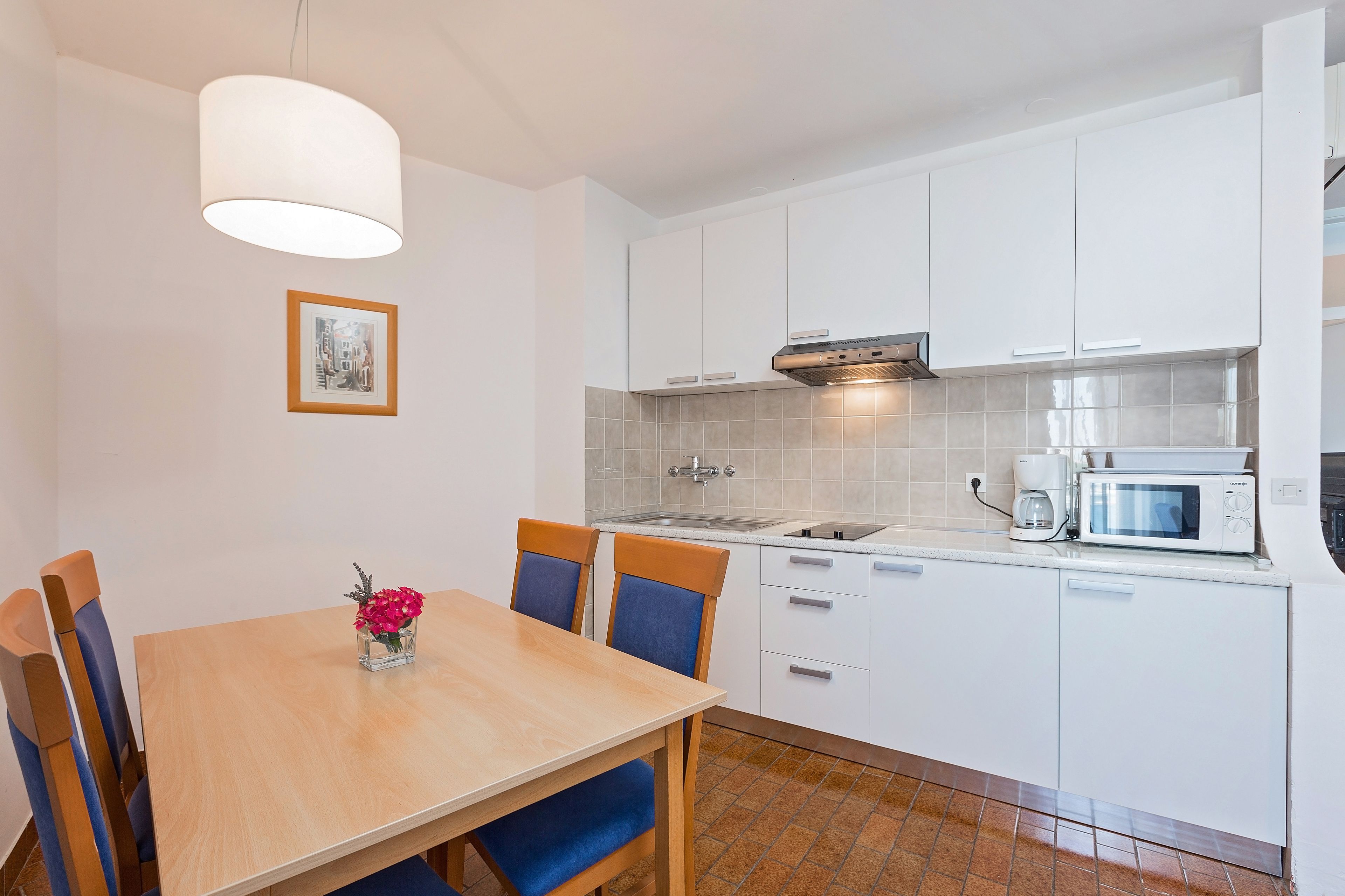 A modern kitchen with white cabinets, a stainless steel range hood, a Bosch coffee maker, and a microwave.