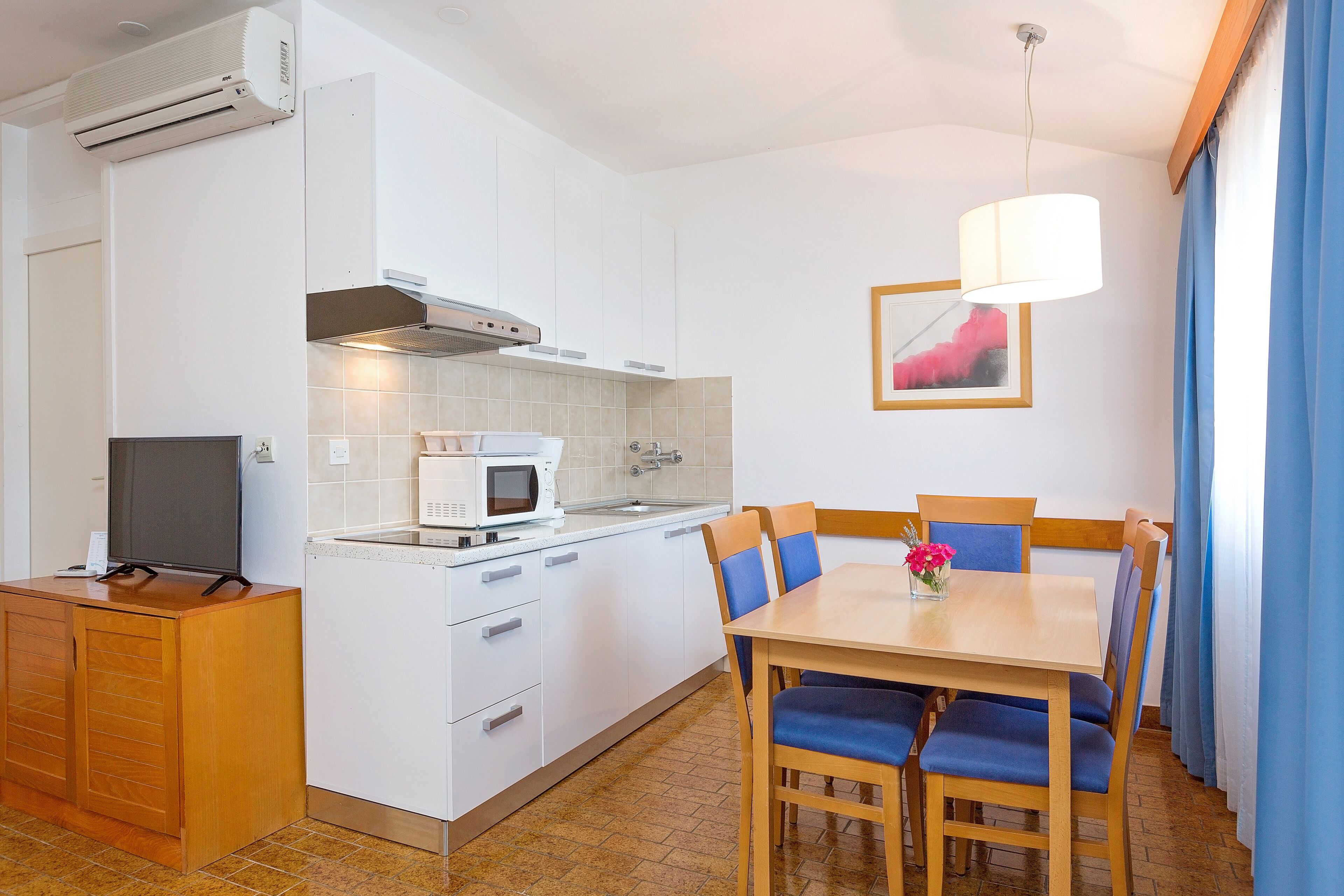 A compact kitchen with a microwave, stove, and sink. There is a dining area with a table and chairs.