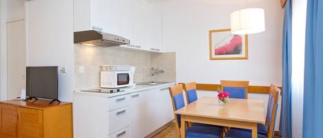 Cocina compacta con microondas, estufa y lavaplatos. Hay un comedor con mesa y sillas.