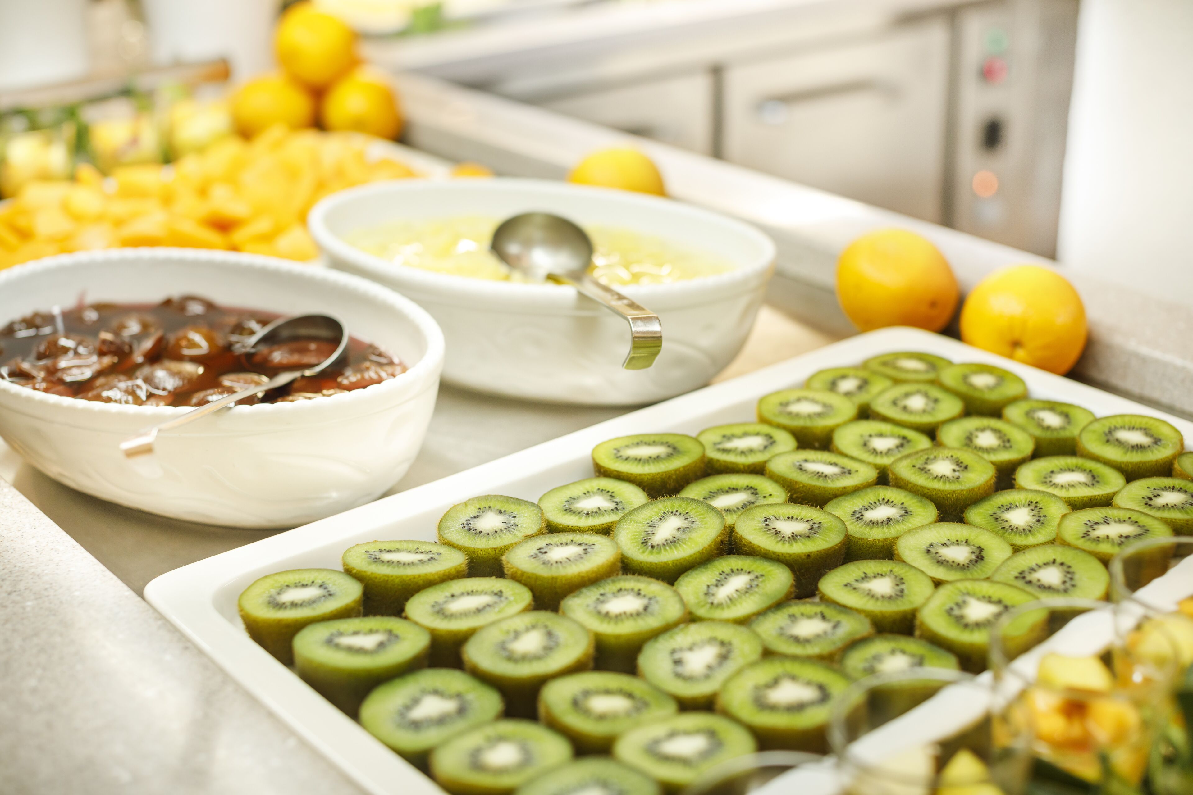 A buffet table with various food items including sliced kiwi, bowls of soup, and a dish with a dark sauce.