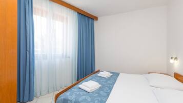 A hotel room with a bed, a wooden headboard, a window with blue curtains, and a wall-mounted light fixture.