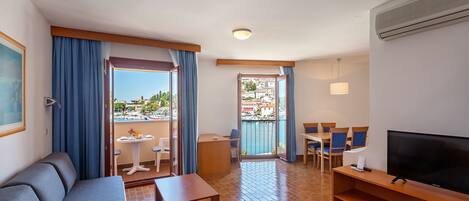 A hotel room with a balcony, a sofa, a TV, a dining table, and chairs.