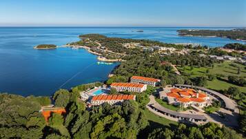 An aerial view of a coastal resort with multiple buildings, a swimming pool, and surrounding greenery.