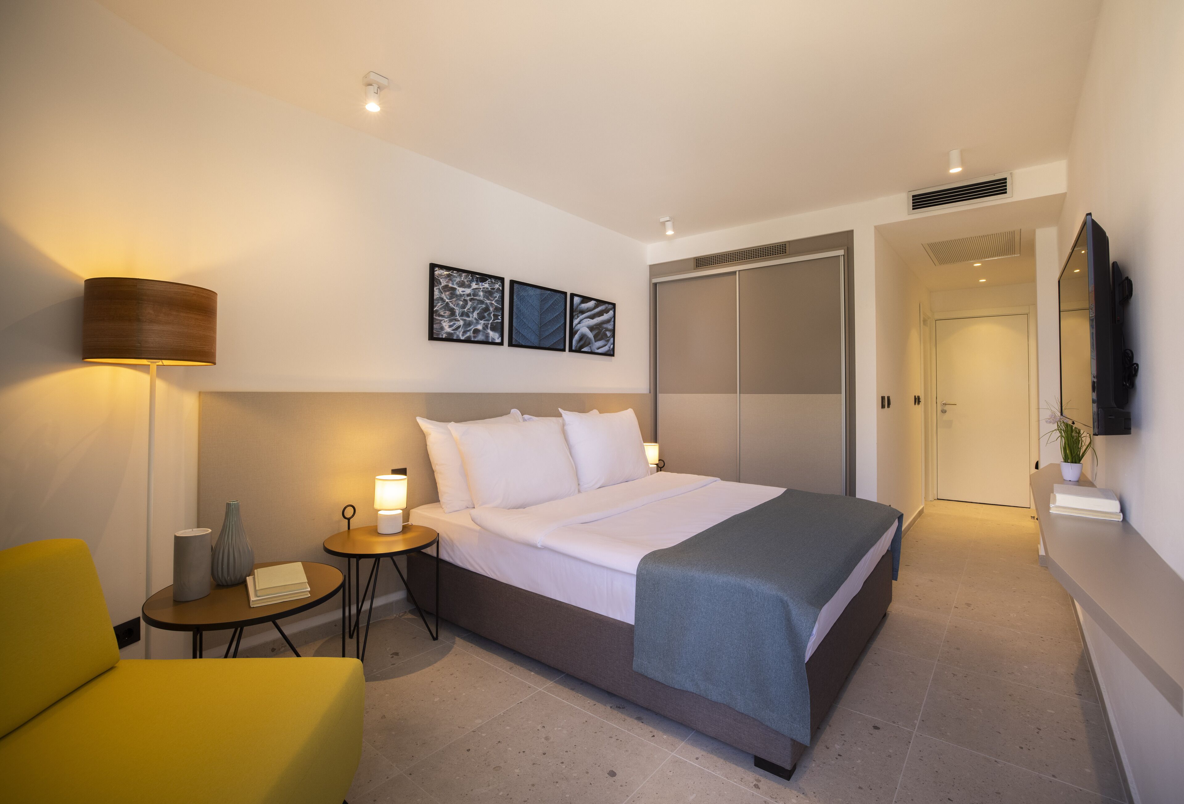 A modern hotel room with a bed, bedside table, lamp, and a small table with a chair.