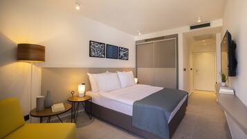 A modern hotel room with a bed, bedside table, lamp, and a small table with a chair.