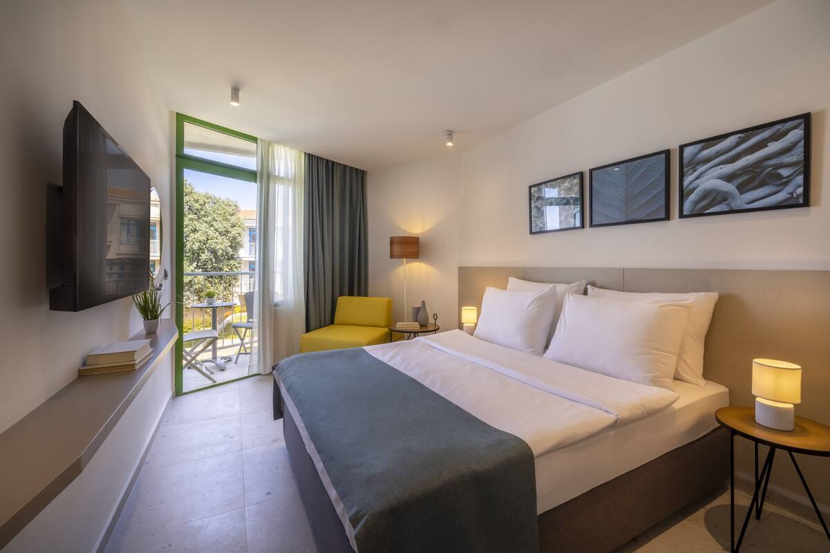 Une chambre d’hôtel avec un lit, une télévision, un bureau, une chaise et un balcon donnant sur la verdure.