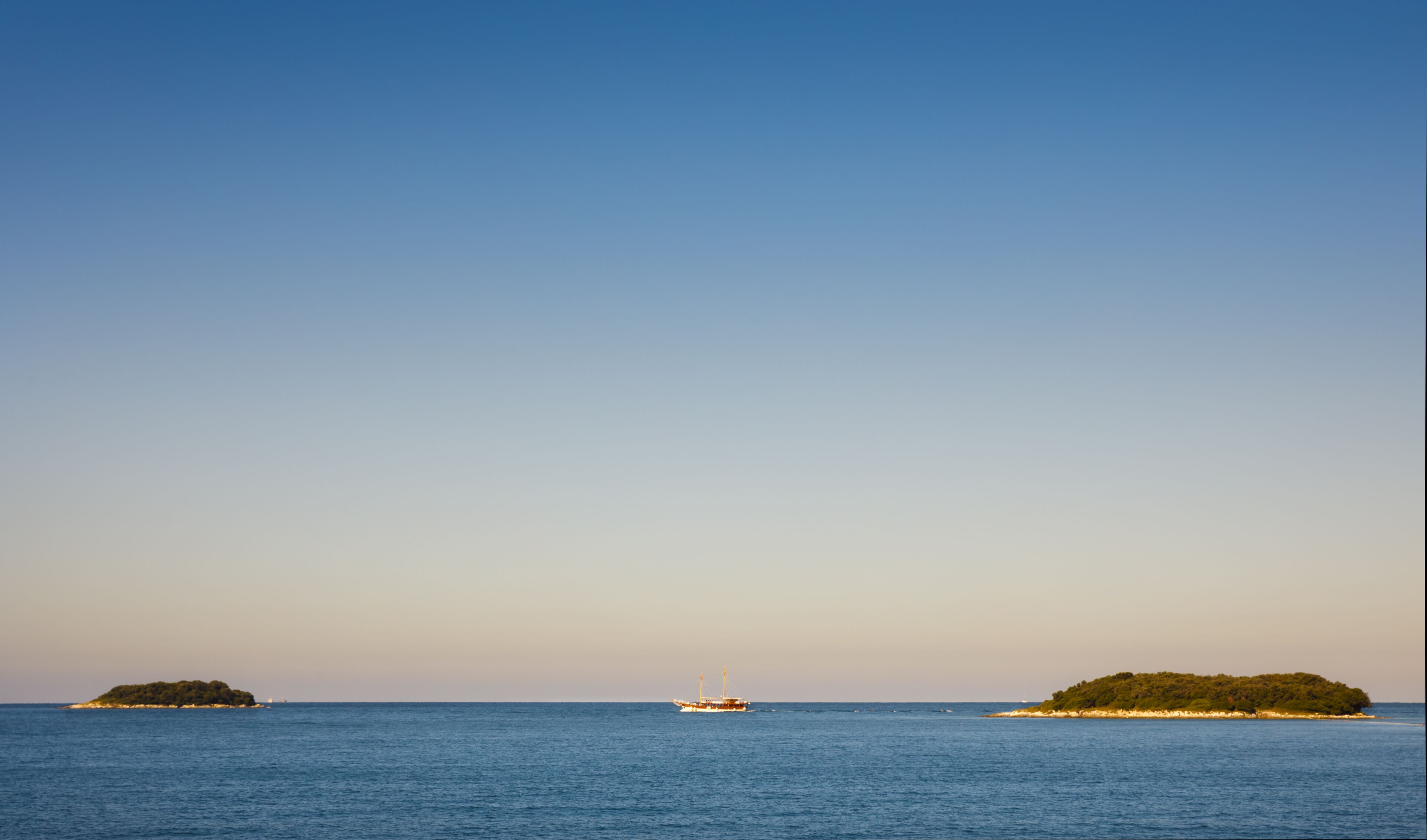 A calm sea with a boat and two small islands.