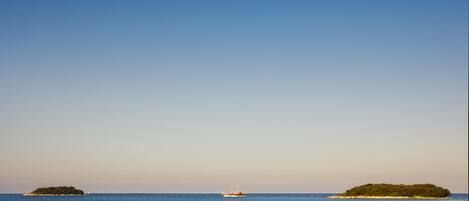 A calm sea with a boat and two small islands.