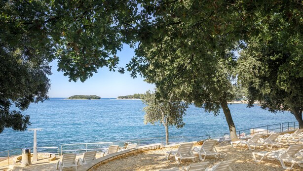 A seaside view with a pebble beach, lounge chairs, and a clear blue sea. - Maistra Select Funtana All Inclusive Resort (Funtana)