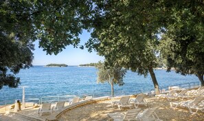 A seaside view with a pebble beach, lounge chairs, and a clear blue sea. - Maistra Select Funtana All Inclusive Resort (Funtana)