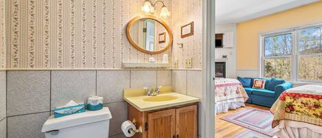 A bathroom with a toilet, sink, and mirror, wooden cabinets, and a window with a view.