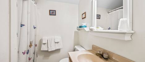 Een badkamer met toilet, wastafel, spiegel en douchegordijn.