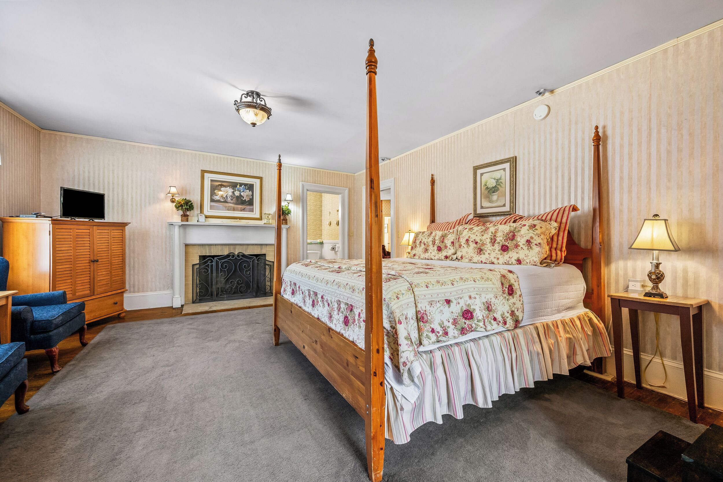 A four-poster bed with floral bedding, a television, a wooden wardrobe, and a fireplace.