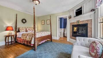 A bedroom with a four-poster bed, a fireplace, a blue carpet, and a white armchair.
