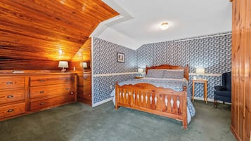 A bedroom with a wooden ceiling, a bed with a wooden headboard, a dresser, and patterned wallpaper.