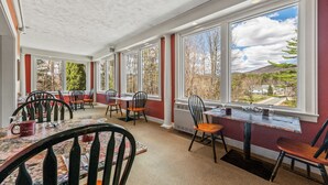 Une véranda avec de grandes fenêtres, des tables et des chaises en bois.