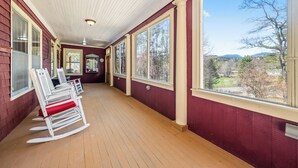 Une véranda couverte avec un plancher en bois, de grandes fenêtres et une vue sur l’extérieur.